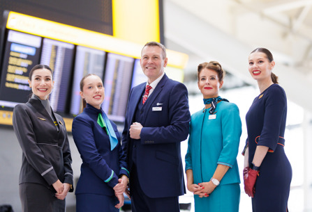 Members of cabin crew of IAG airlines posing by screens at Heathrow